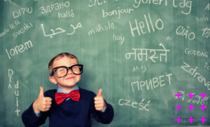 Menino sorri na frente de uma lousa com palavras em diversos idiomas.