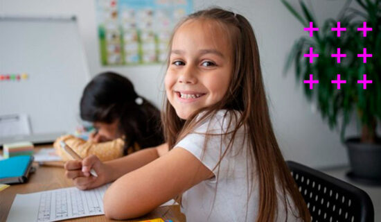 criança sorridente sentada à mesa fazendo atividades de alfabetização