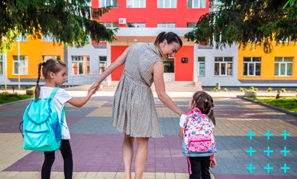 mãe levando suas duas filhas para a escola enquanto segura as crianças em cada mão.