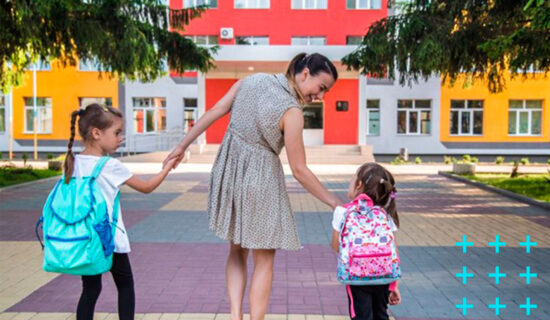 mãe levando suas duas filhas para a escola enquanto segura as crianças em cada mão.