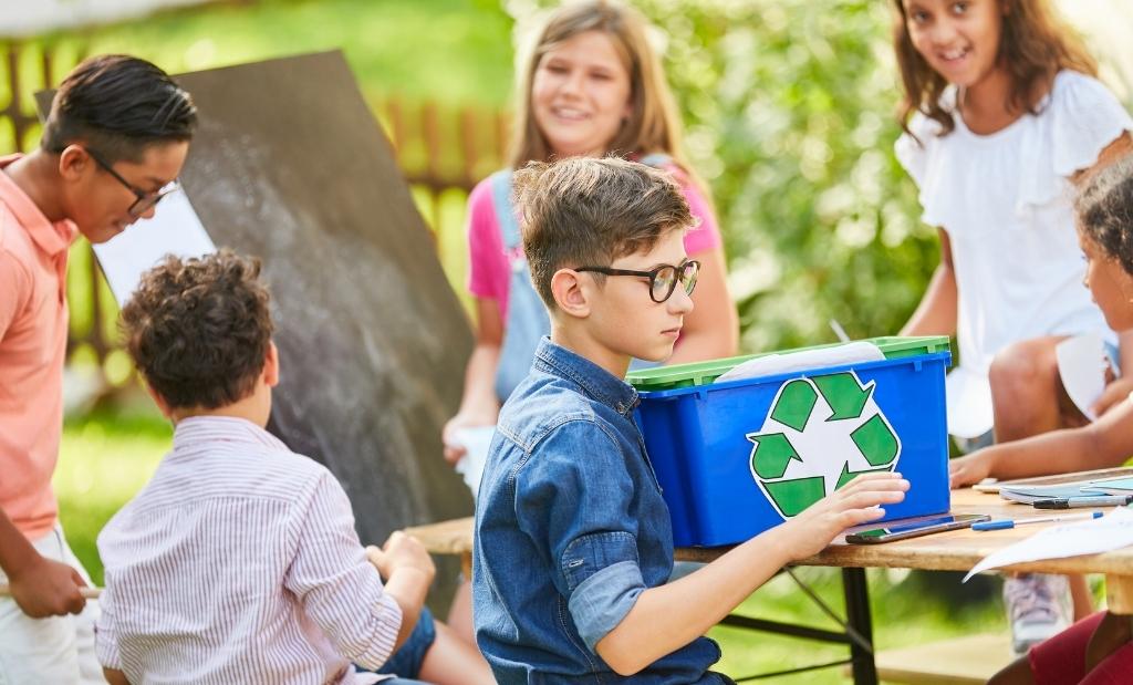 alunos reunidos ao redor de caixa de reciclagem durante atividade ambiental.