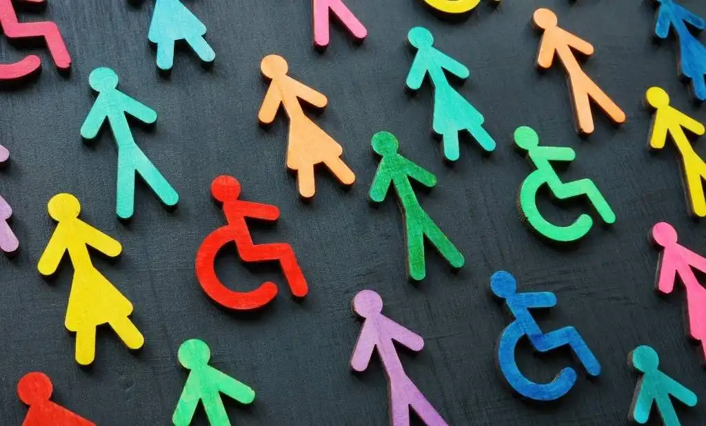 Imagem com figuras de papel coloridas representando diversidade e inclusão, incluindo símbolos de acessibilidade para pessoas com deficiência, em fundo escuro.