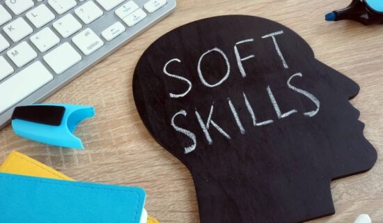 placa preta com a inscrição "soft skills" sobre uma mesa de trabalho com teclado e materiais escolares.