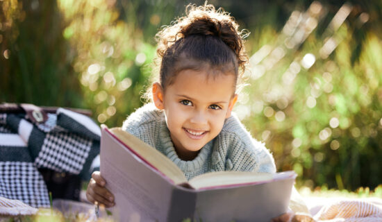 Uma garotinha lendo um livro enquanto relaxava em um parque ou jardim.