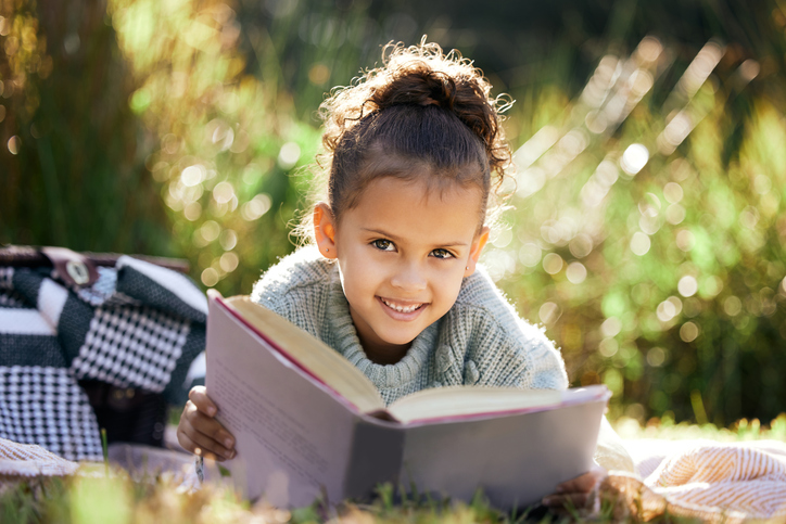 Uma garotinha lendo um livro enquanto relaxava em um parque ou jardim.