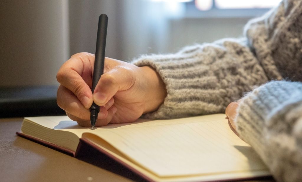 pessoa escrevendo em caderno com caneta preta.